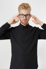 Young man in thinking process. Close up redheaded guy with red beard in black shirt, glasses focus...