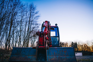 Heavy duty industrial machine parked in countryside at dusk alongside leafless trees in a close up...