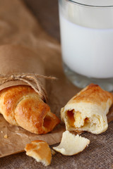 Croissants with jam whole and broken with crumbs and a glass of milk on burlap tablecloth.