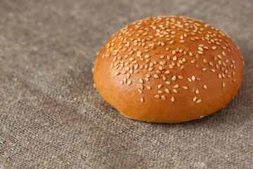 Bun with sesame seeds, round one on the rough burlap tablecloth.