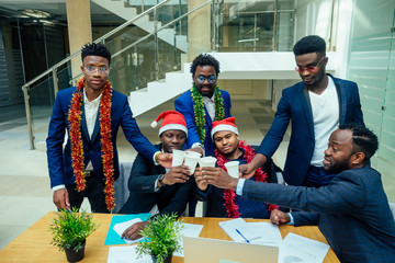happy group of indian and african american people drinking toast from cup,wearing santa hat and tinsel