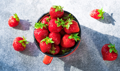 Fresh Strawberries in red enamel cup on grey background.