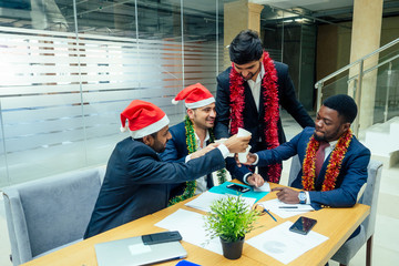 happy group of indian and african american people drinking toast from cup,wearing santa hat and tinsel