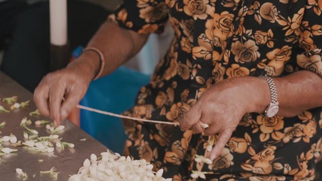 An Indian woman strings garlands of freshly flowers at the flower market. Making flower necklaces, wreath