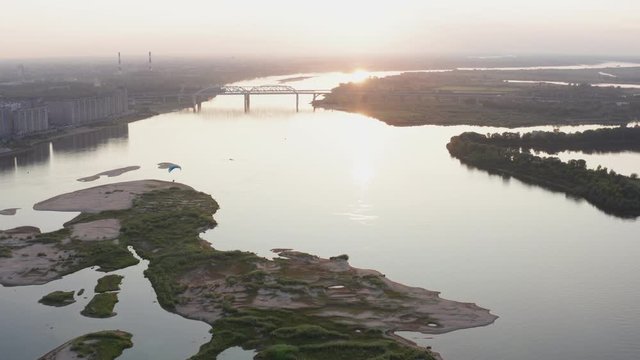 Parasail wing flying on golden sunset horizon landscape. Paraplane flying over river on city architecture background. Paraglider parachute sport aerial view
