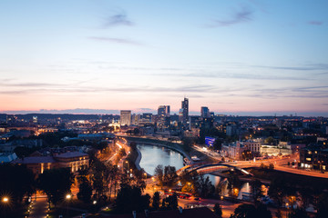 Vilnius business district skyline panorama with Neris river and Mindaugas bridge at night during golder hour sunset