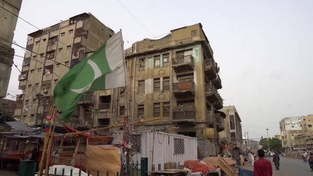 Karachi Waving Pakistan Flag at a Street in a Residential Area with Busy Traffic and Walking People on a Cloudy Day