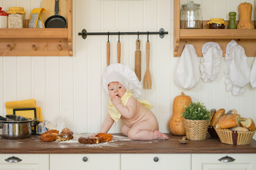 little baker baby child in chef hat at kitchen table alone with orange big pumpkin 