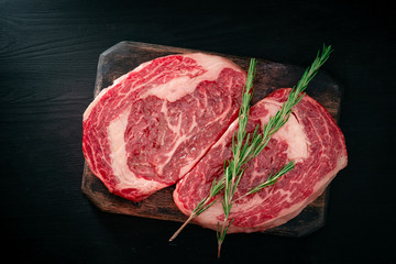 Ideal raw rib eye beef steak with rosemary on black wooden background, top view and copy space