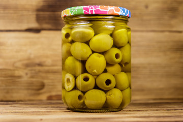 Pickled green olives in glass jar on wooden table
