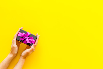 hands holding present in box on yellow background top view copyspace