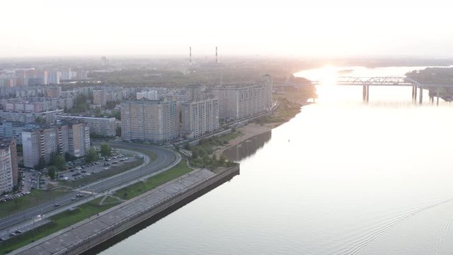Aerial landscape golden sunset in city sky. Eveining city panorama from drone above. Urban architecture and highway in modern city on river shore.