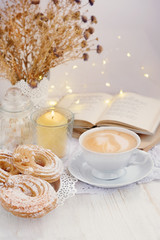 coffee Cup, books, garland and donuts in cozy interior. Evening still life with Cup of coffee and candles on wooden table. Spending weekend in cozy home. delicious Breakfast or lunch with coffee.