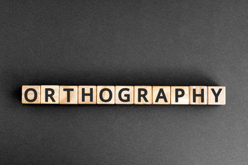 orthography - word from wooden blocks with letters, orthography concept, random letters around, grey background