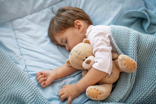 Sleepyhead. Young boy peacefully sleeping on a blue pillow. Baby needs his sleep! Baby boy sleeping with teddy bear and pacifier. Baby sleeping covered with soft blanket
