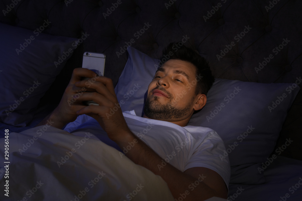 Wall mural Handsome man using smartphone at night. Bedtime