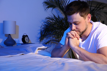 Handsome man saying bedtime prayer in dark room at night. Space for text