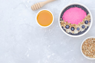 Smoothie bowl with fruits and granola and honey on a gray background.