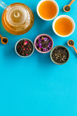 Tea in pot and cups with dry leaves on blue background top view mock up