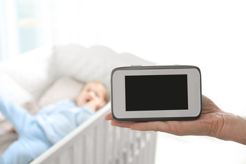Woman holding baby monitor near crib with child in room. Video nanny