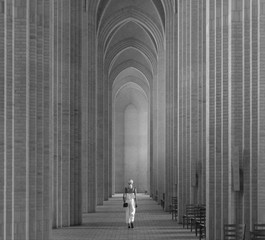 a woman is walking down the long archways of the cathedral