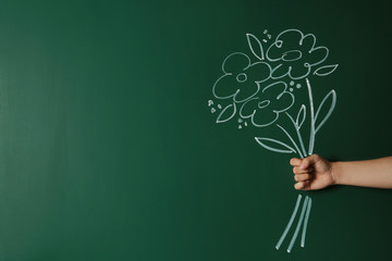 Closeup view of woman with drawn flowers on green chalkboard, space for text. Teacher's day
