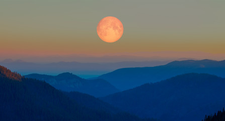 Beautiful landscape with blue misty silhouettes of mountains against full moon 