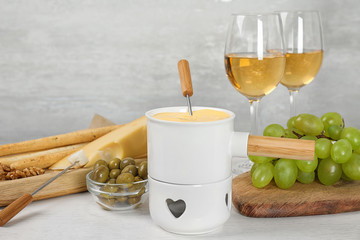 Pot of tasty cheese fondue and products on white wooden table