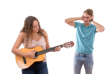 Fototapeta premium Caucasian young girl playing guitar bothering her brother or partner in white background isolated