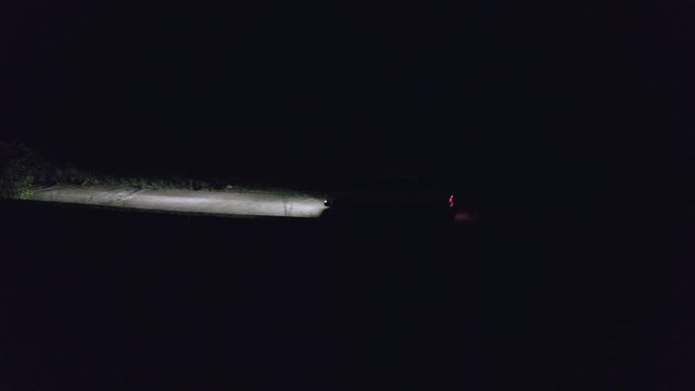 Car moving on countryside road in dark night drone view. Car headlights illuminating night road in darkness. Night car motion aerial view