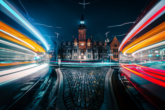 Light streaks as cars move quickly in front of a stone building.