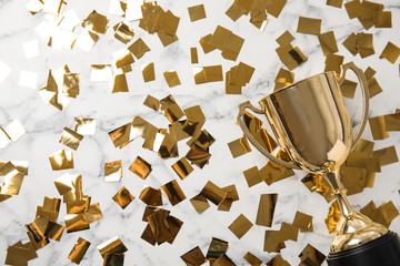Gold trophy cup and confetti on marble background, flat lay. Space for text