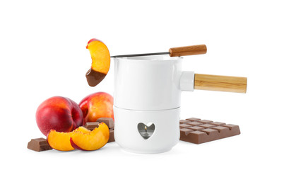 Fondue pot with chocolate and fresh peaches on white background