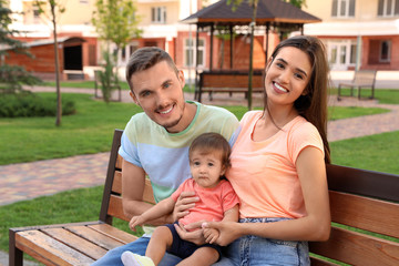 Happy family with adorable little baby on bench outdoors