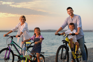 Obraz premium Happy family with children riding bicycles near river at sunset