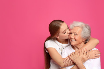 Young woman kissing her grandmother on pink background. Space for text
