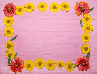 yellow and orange flowers with green leaves pink wooden background texture tree top view