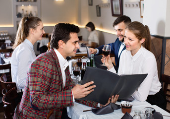 Сheerful friends choosing dishes out of menu card in restaurant