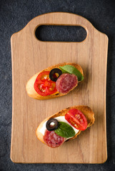 Open faced sandwich canape or crostini on a wooden serving board on dark stone  background closeup. Top view.