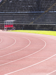 Red running tracks in an antique stadium with red chairs and concrete grandstand in the background.;
