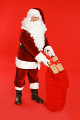 Authentic Santa Claus with sack and gift on red background