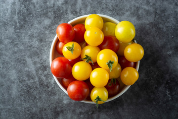 Yellow and red tomatoes in plate, isolated over dark background.