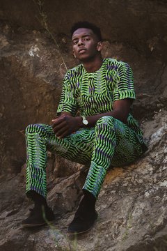 Stylish man wearing patterned shirt and pants sitting on rock