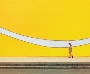 Woman walking across a walkway with abstract mural wall next to her.
