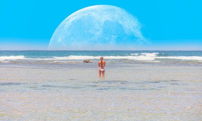 Blond woman taking self portrait at the beach with full moon "Elements of this image furnished by NASA"