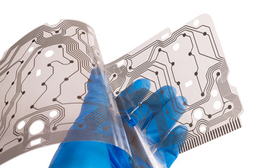 Plastic flex printed circuit board in a human palm isolated on white background. Hand of engineer in blue glove holding a bent membrane of dismantled computer keyboard with brown copper layer of PCB.
