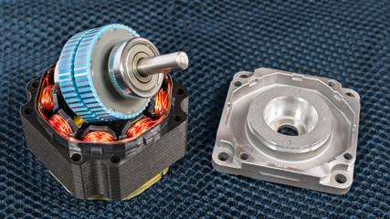 Disassembled electric step motor parts on a dark grid background. Blue rotor with steel shaft on...