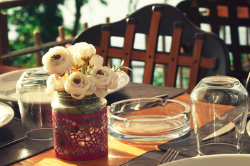 Served table in a summer cafe. The sea in the background. Wooden furniture, white flowers.