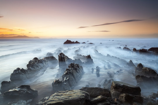 Rock formation at barrika beach in spain. Water flowing around rocks at sunset. Misty water long exposure shot. Very dramatic and moody fineart landscape photo.