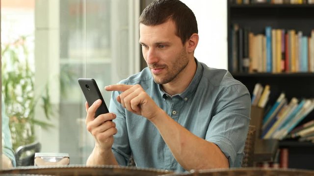 Excited man checking smart phone finding good news in a coffee shop